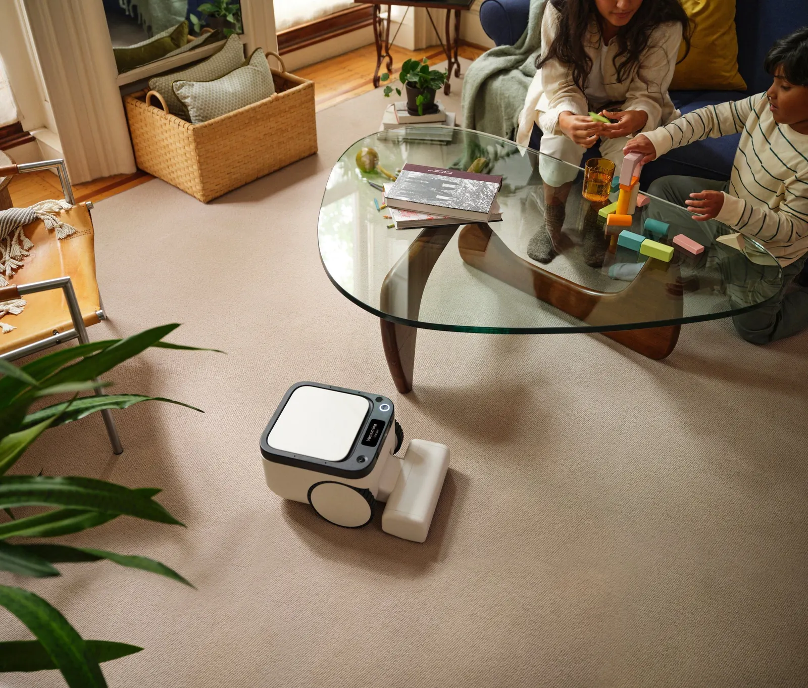 Matic press photograph: the Matic robot cleaning a living-room rug while two children play at a glass coffee table.